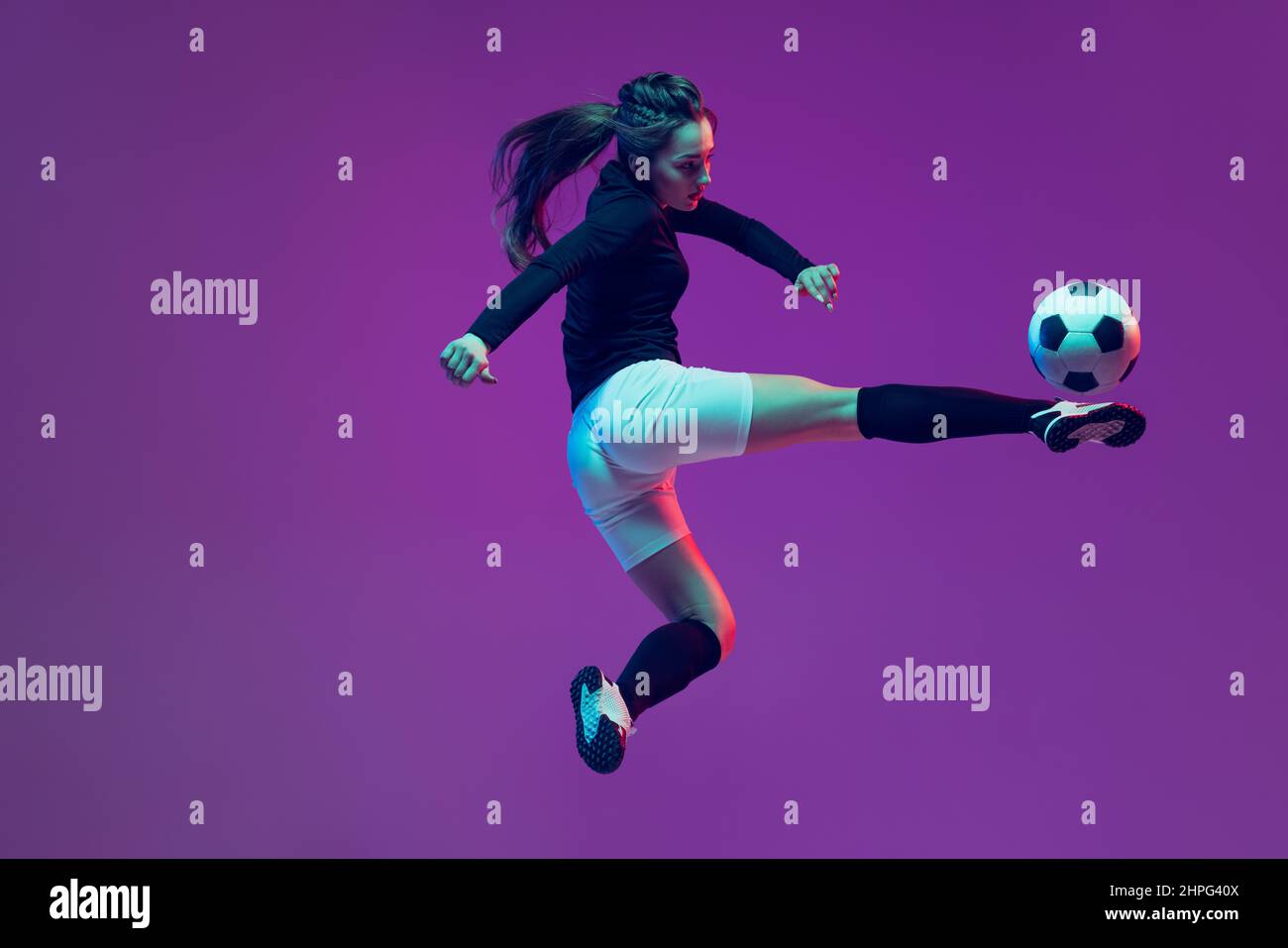 In action. One sportive girl, female soccer player training with football ball isolated on purple studio background in neon light. Sport, action Stock Photo
