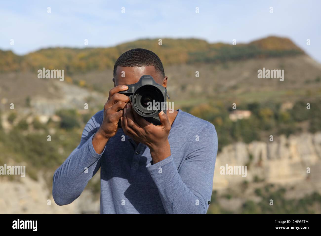 Front view portrait of a man with black skin taking photos with dslr camera in nature Stock Photo