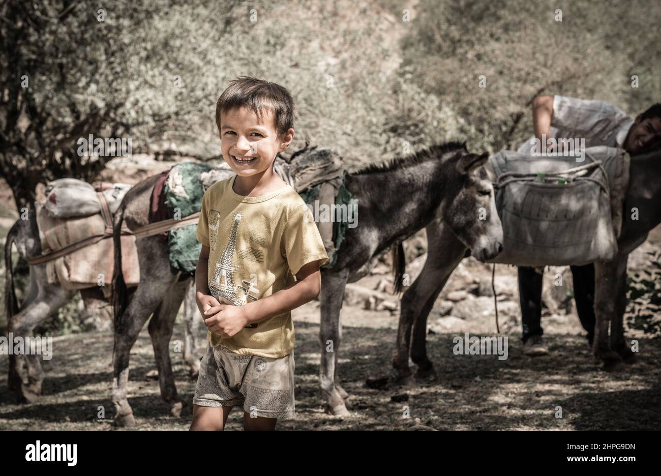 August 25, 2016, Shirkent Valley, Tajikistan: Local boy is posing for the camera as his father attending to pack mules in the background Stock Photo