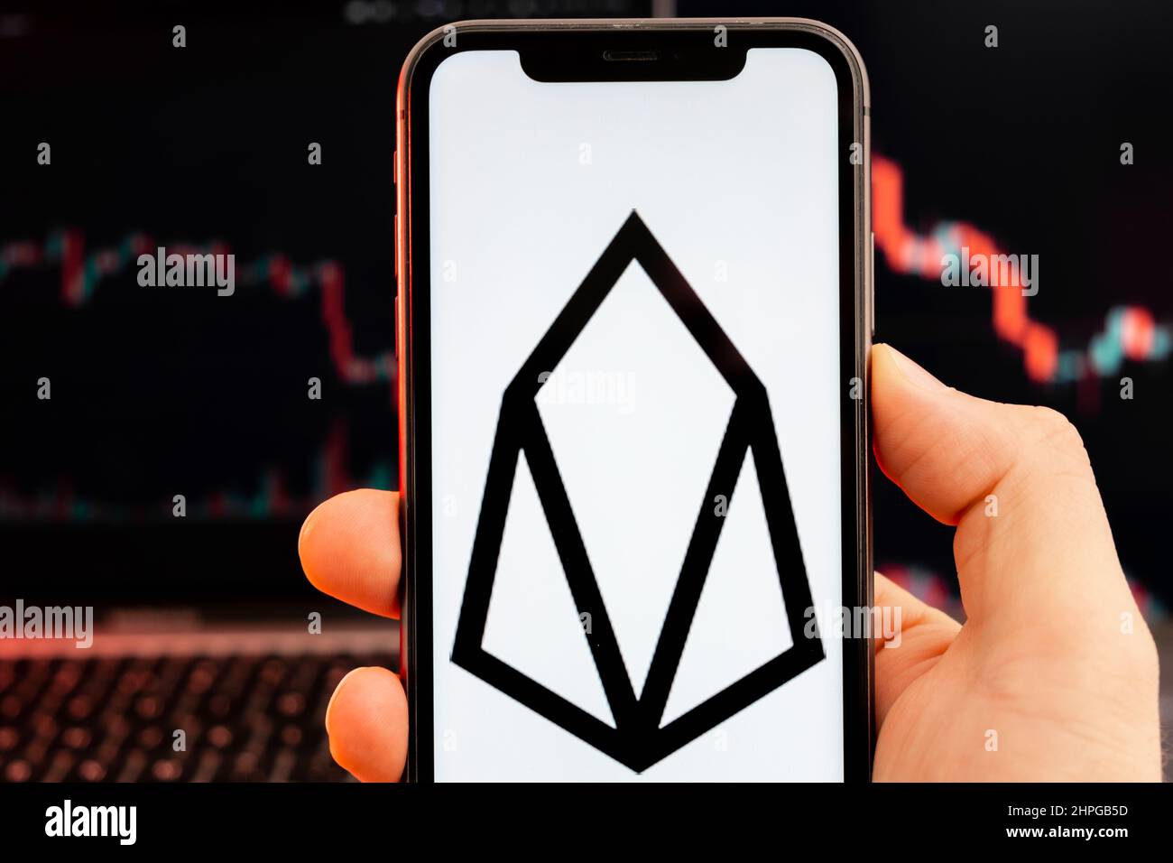 EOS app of cryptocurrency stock market analysis on the screen of mobile phone in man hands and downtrend charts trading data on the background, February 2022, San Francisco, USA. Stock Photo