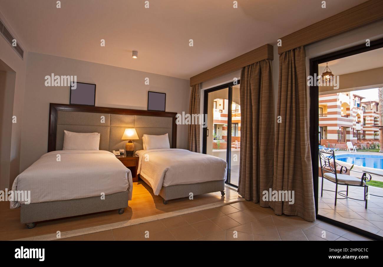 Twin beds in suite of a luxury hotel room with terrace and pool view Stock Photo