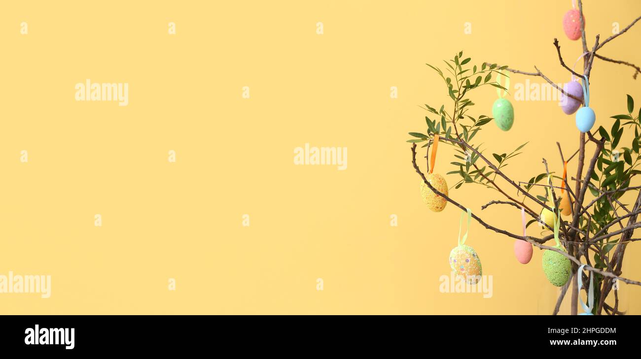 Easter eggs hanging on tree branches against color background with space for text Stock Photo
