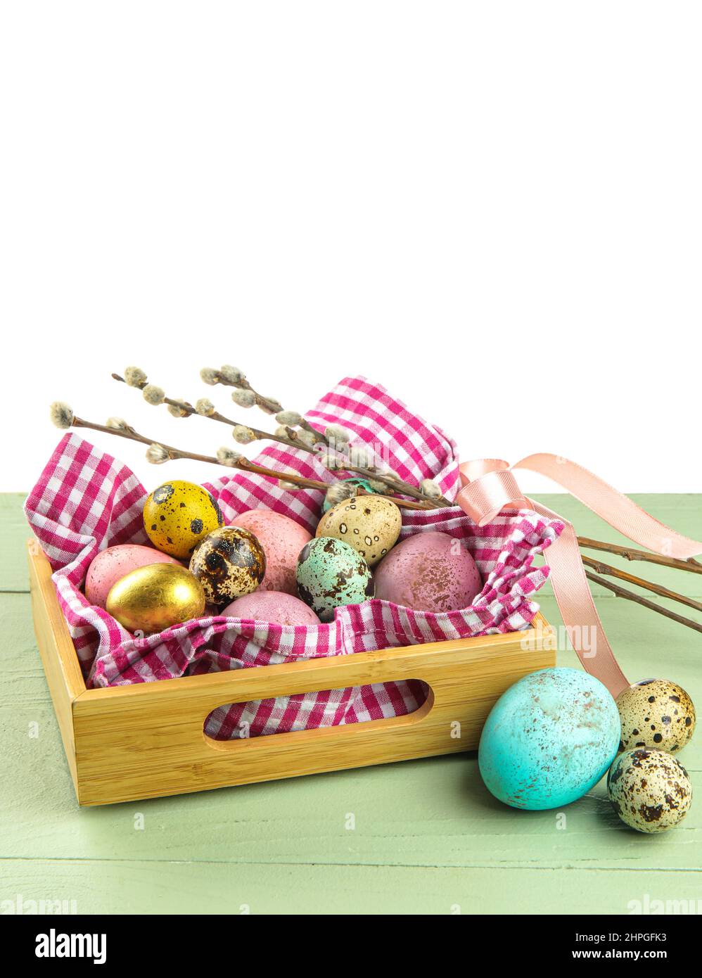 Box with painted Easter eggs and pussy willow on table against white ...