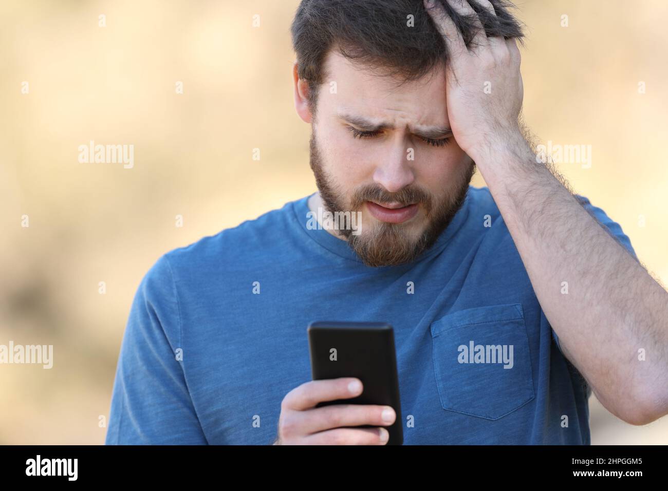 Front view portrait of a worried man checking smartphone outdoors Stock Photo