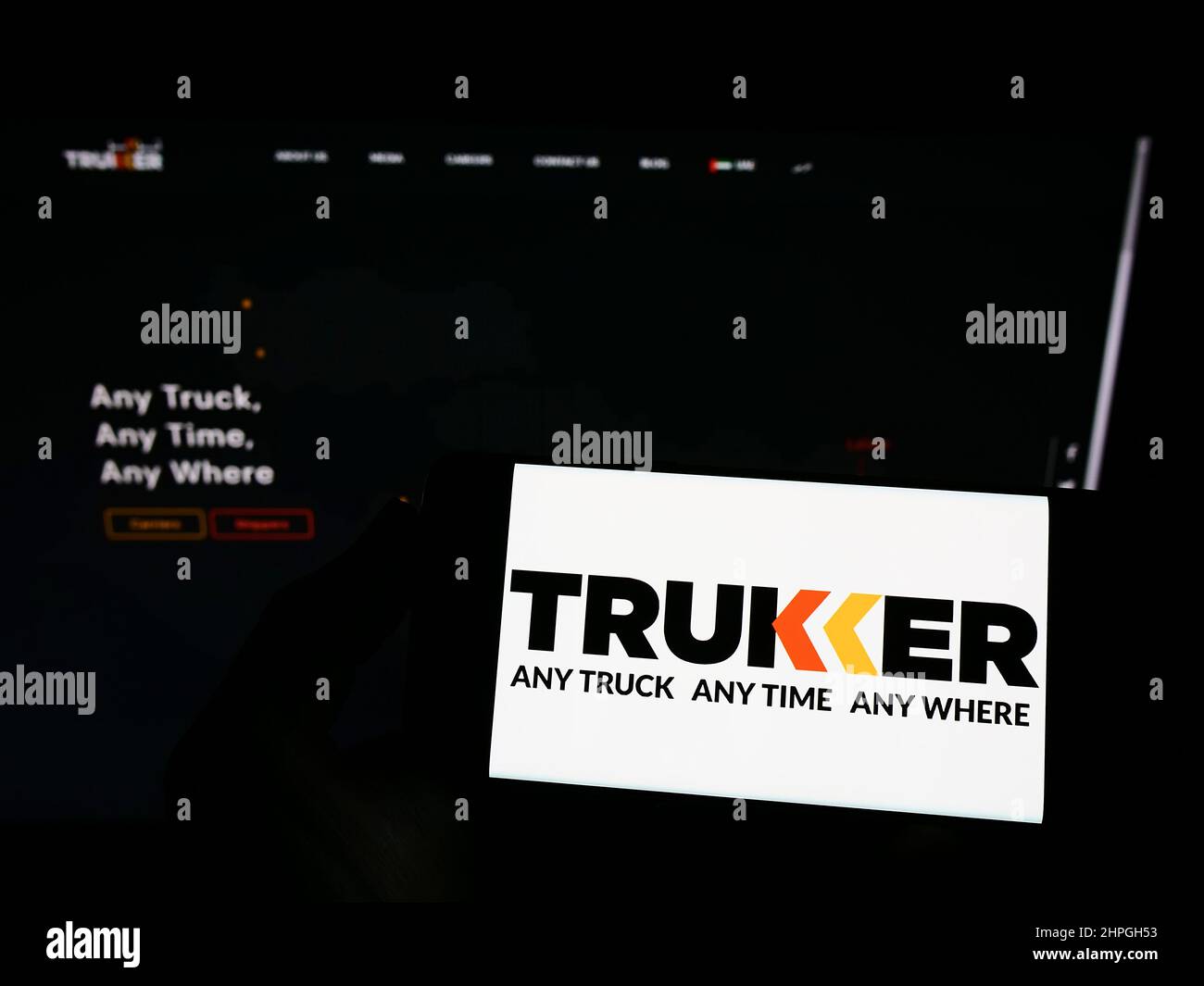 Person holding smartphone with logo of logistics company TruKKer Holding Limited on screen in front of website. Focus on phone display. Stock Photo
