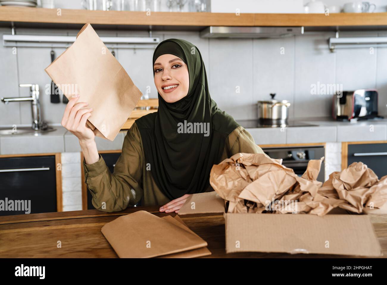 Young muslim woman wearing hijab separating waste while sitting at ...