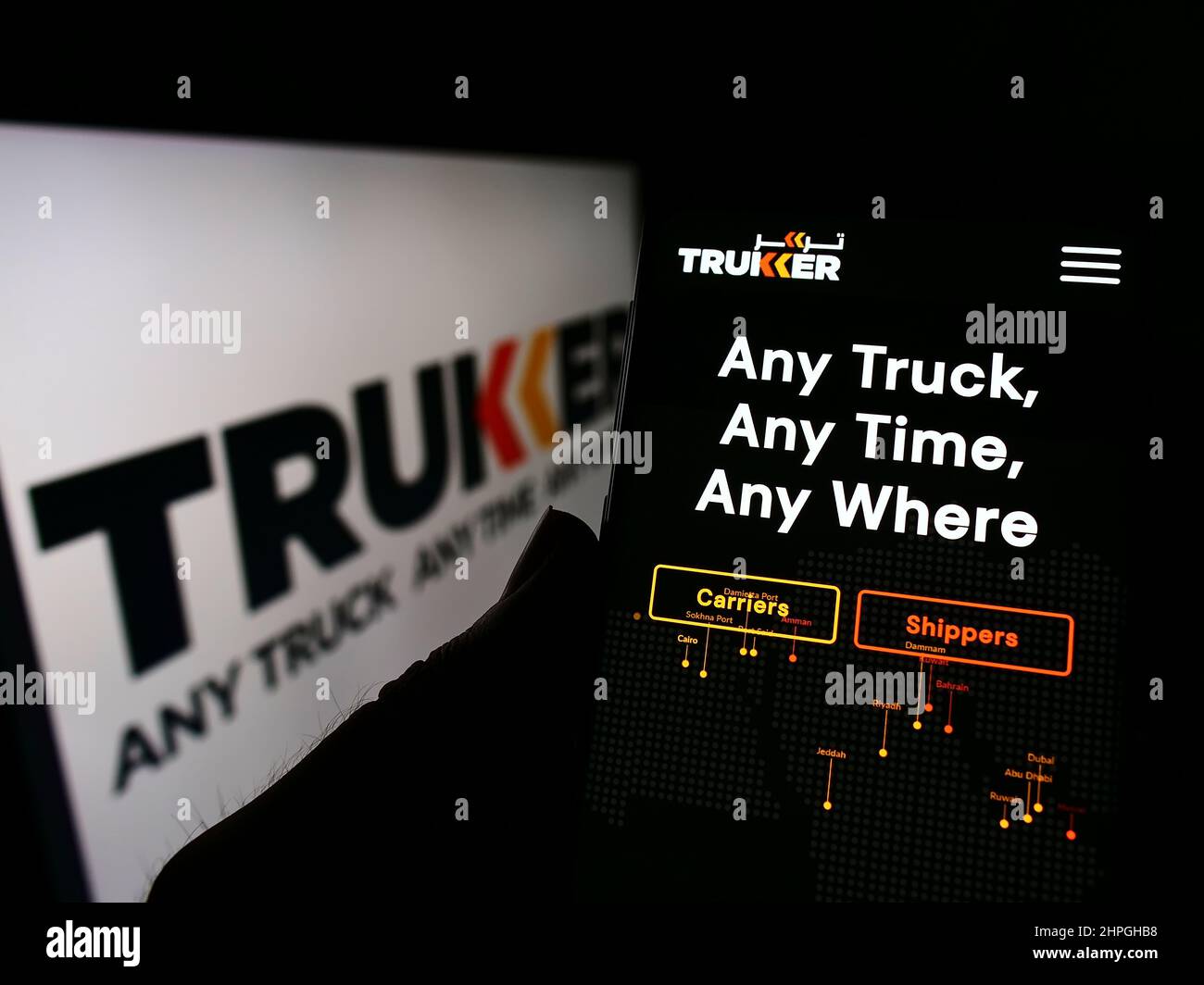 Person holding cellphone with website of logistics company TruKKer Holding Limited on screen in front of logo. Focus on center of phone display. Stock Photo