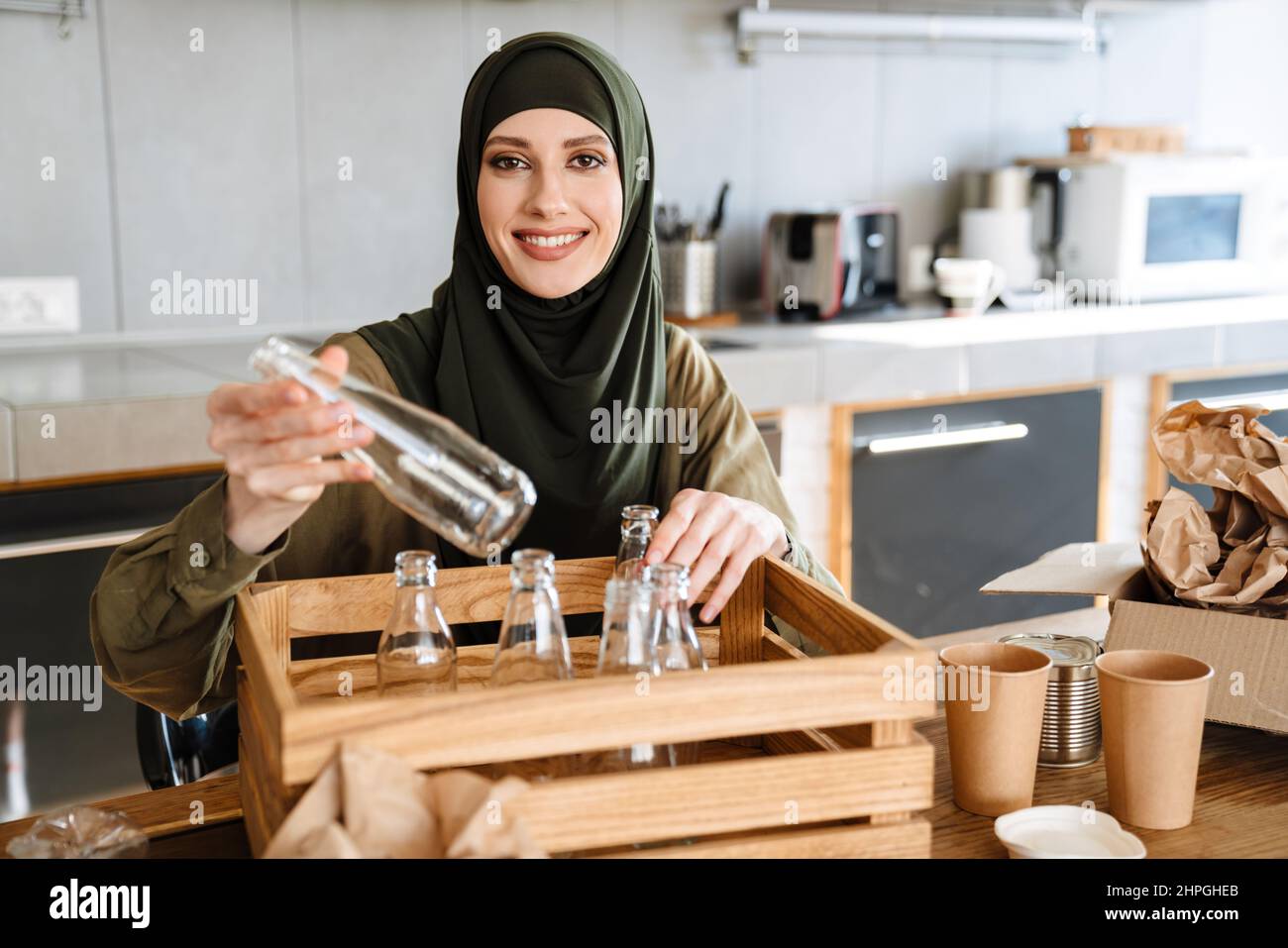 Young muslim woman wearing hijab separating waste while sitting at ...