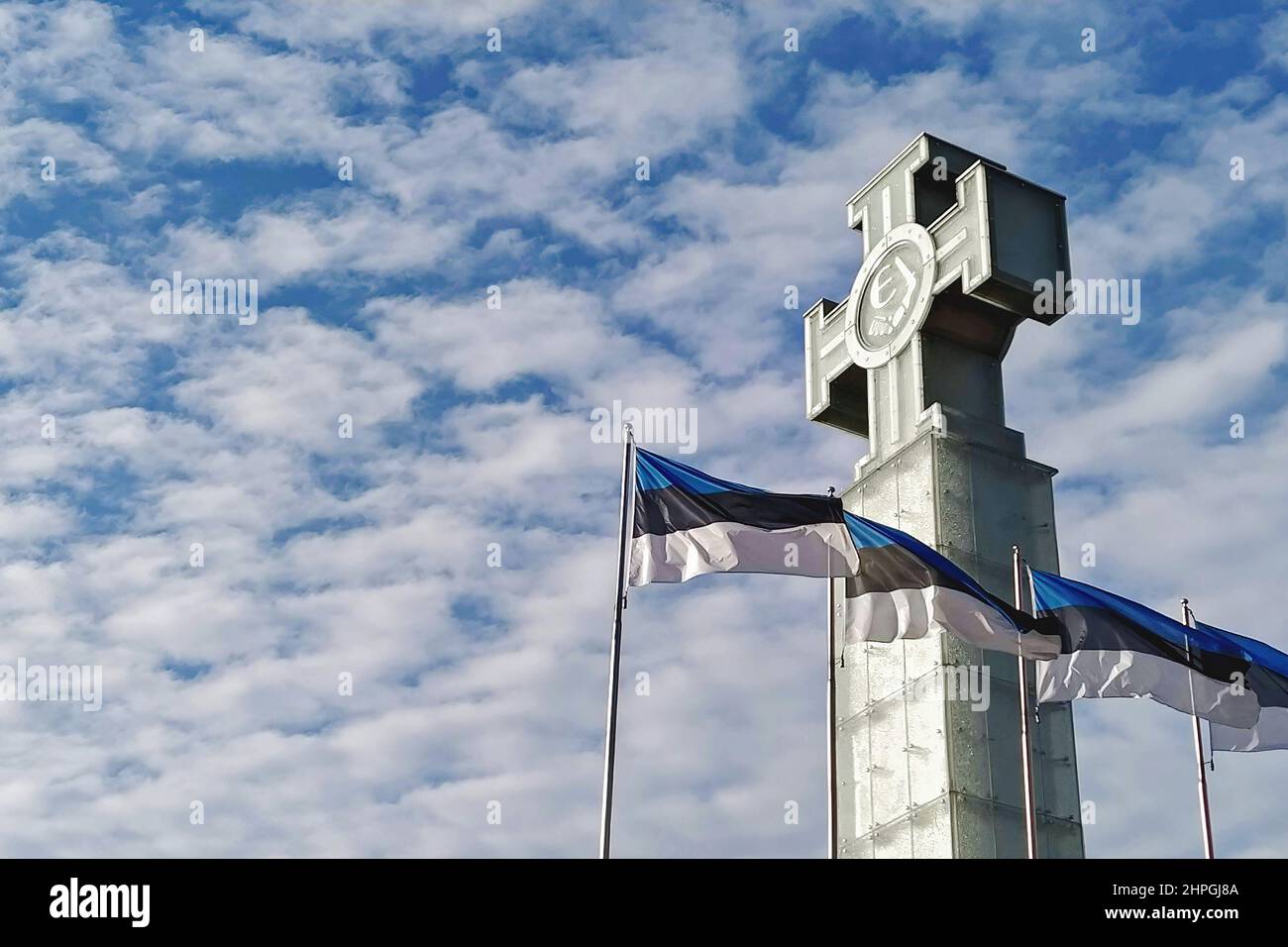 Waving flags of Estonia on blue sky and monument to fallen in War of ...
