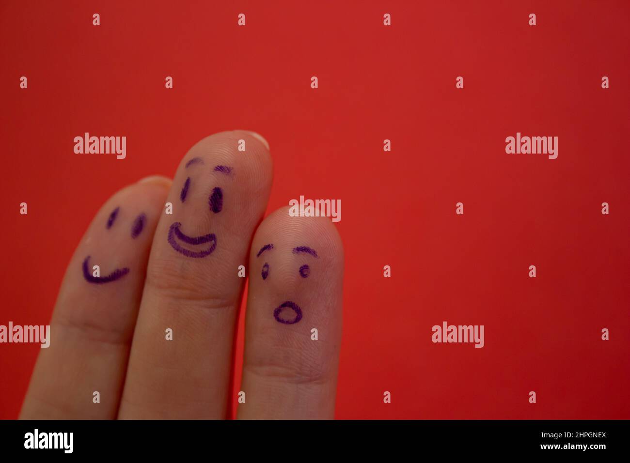 Smiley and shocked faces drawn on fingers isolated on red background
