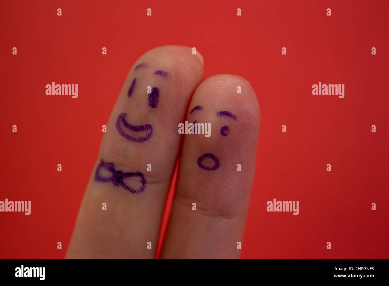 Smiley and shocked faces drawn on fingers isolated on red background. Funny facial expressions on fingers. Stock Photo