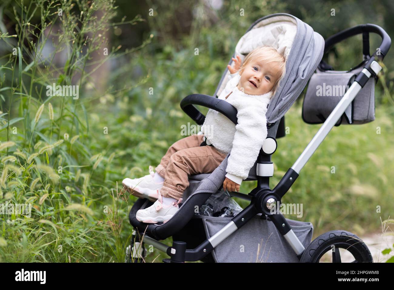 Sweet caucasian baby girl one year old sitting in stroller outdoors at