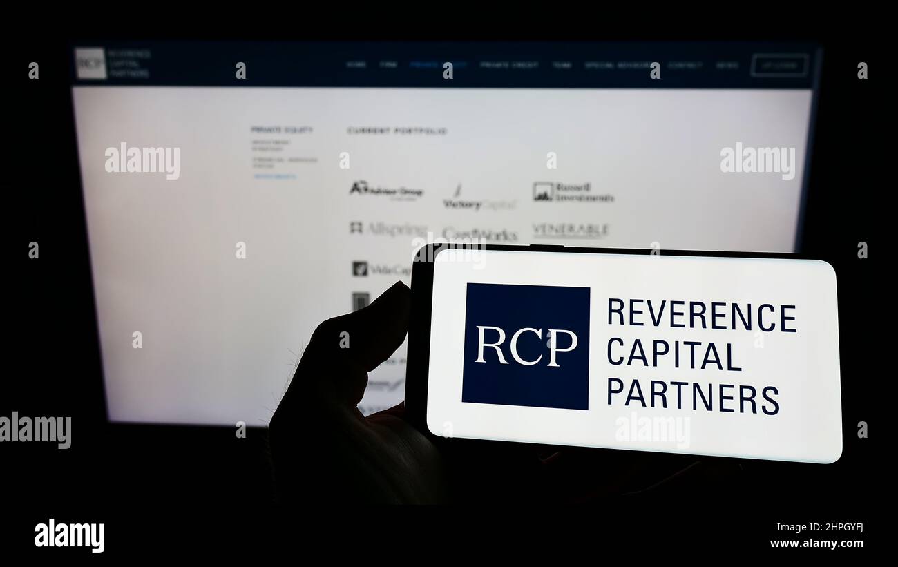 Person holding cellphone with logo of US company Reverence Capital Partners L.P. (RCP) on screen in front of webpage. Focus on phone display. Stock Photo