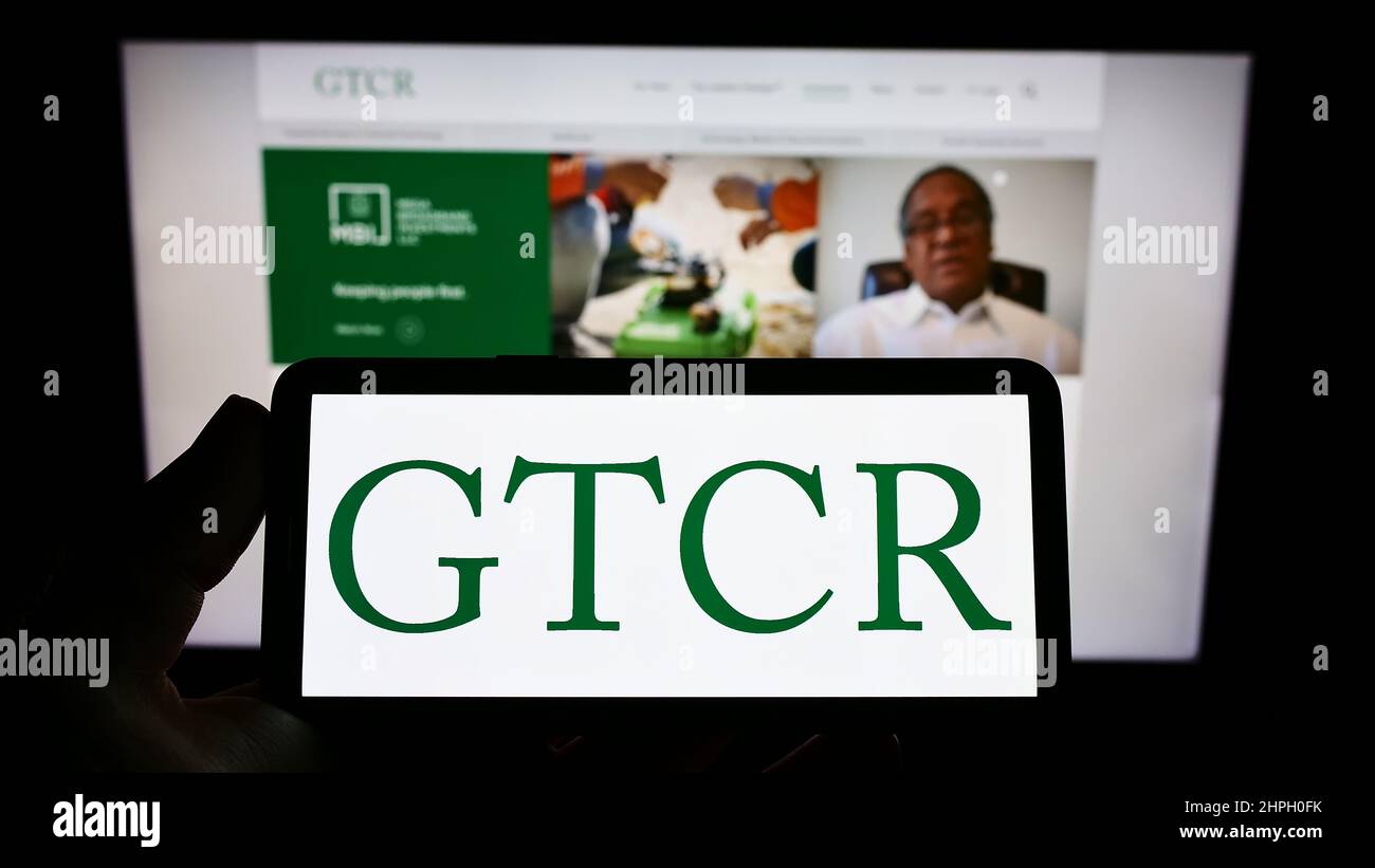 Person holding smartphone with logo of US private equity company GTCR LLC on screen in front of website. Focus on phone display. Stock Photo