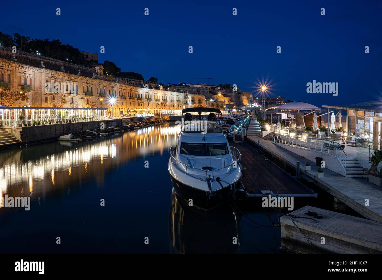 Valletta waterfront district with small harbor with boats and cafes and restaurants illuminated at night. Stock Photo