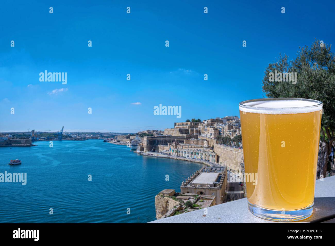 Glass of light beer with view of city wall and harbor in Valletta, Malta. Stock Photo