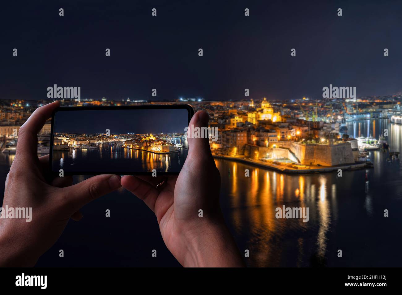 Tourist taking photo of Three cities in Malta at night. Photo taken from Valletta. The Grand Harbour illuminated at night. Stock Photo
