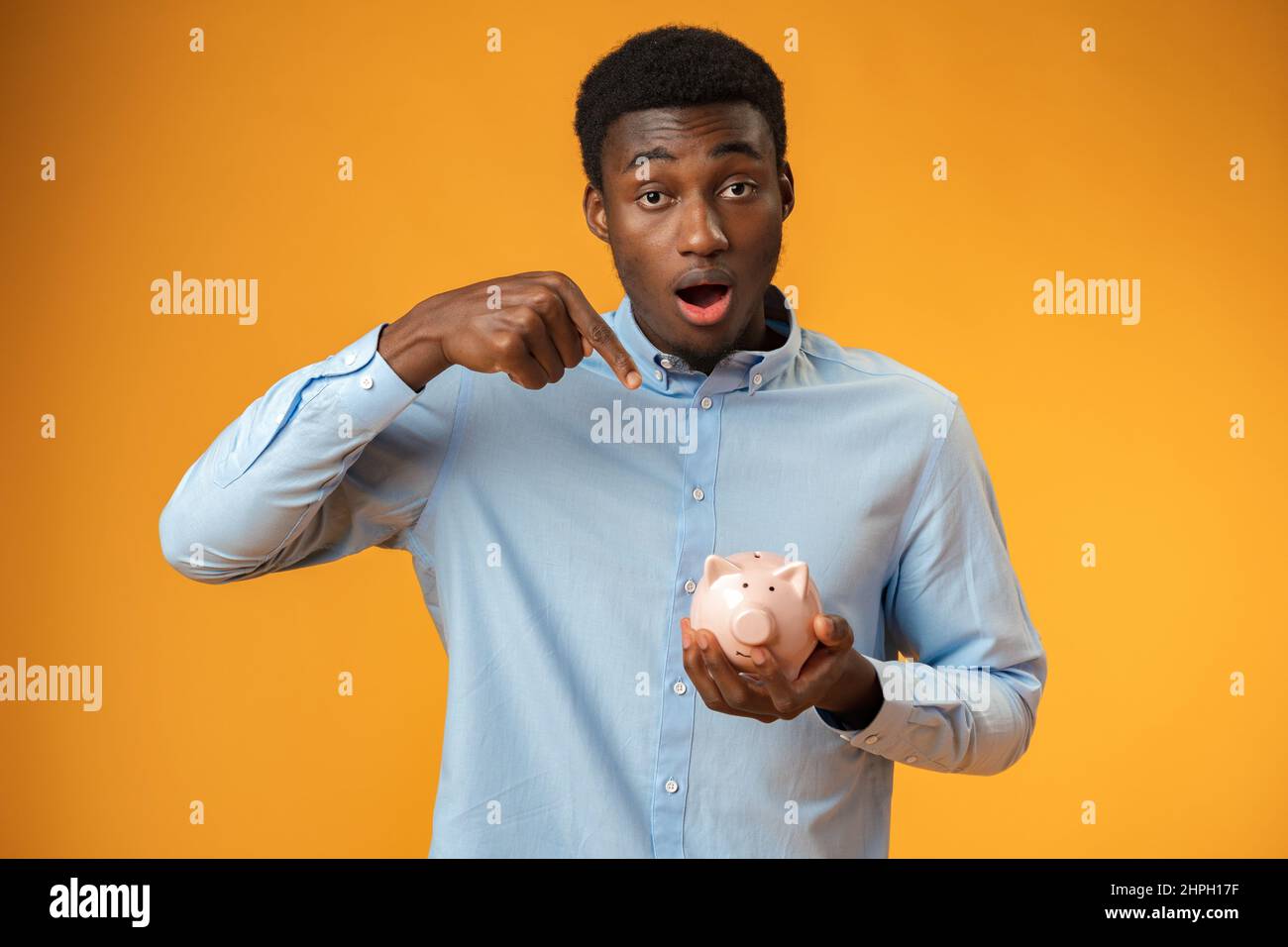 Young african amercian man holding piggy bank over yellow background Stock Photo