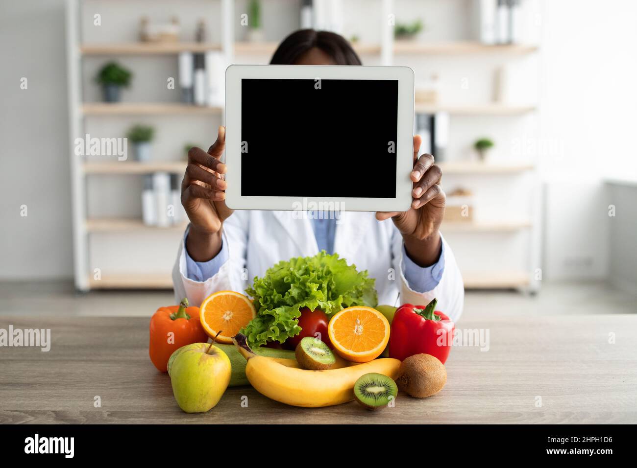 Black nutritionist holding digital tablet with blank screen, demonstrating mockup for website or app design Stock Photo