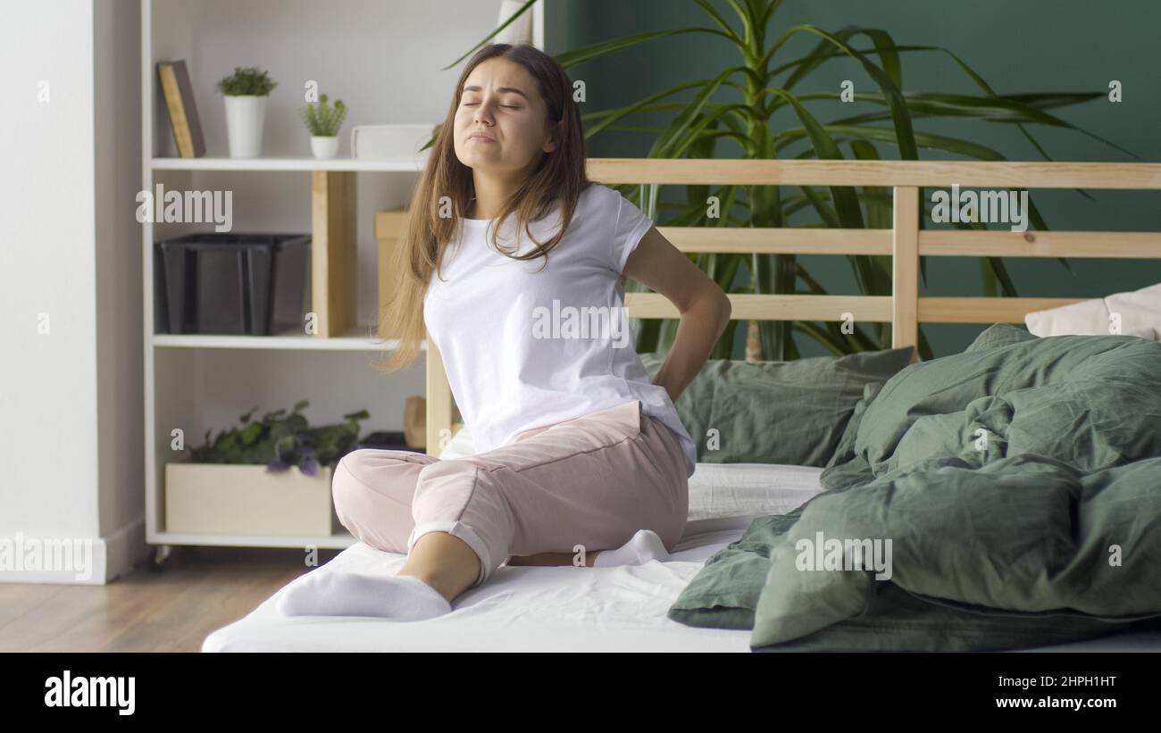 Young Woman Feels Back Pain on the Bed at Home, Rubs Her Lower Back