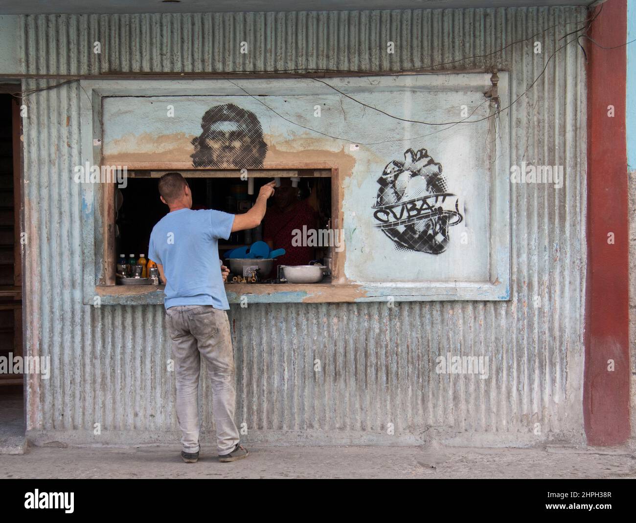 Man at a shop buying goods with a mural of Cuban hero Che Guevara on window sill. Stock Photo