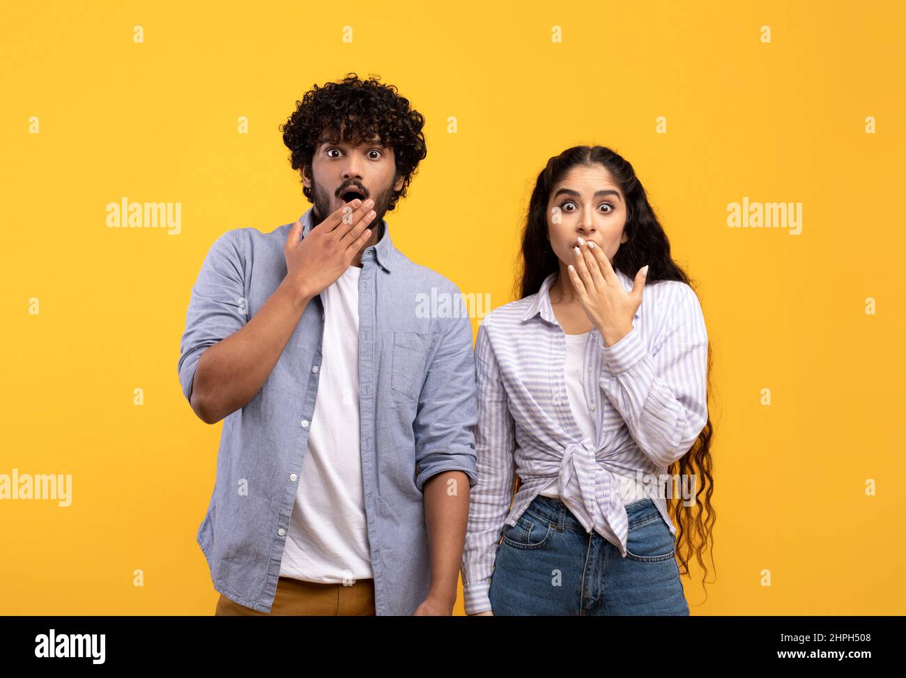 Shocking news, unexpected events. Young indian female and man with wide open eyes, covering mouth with hand Stock Photo