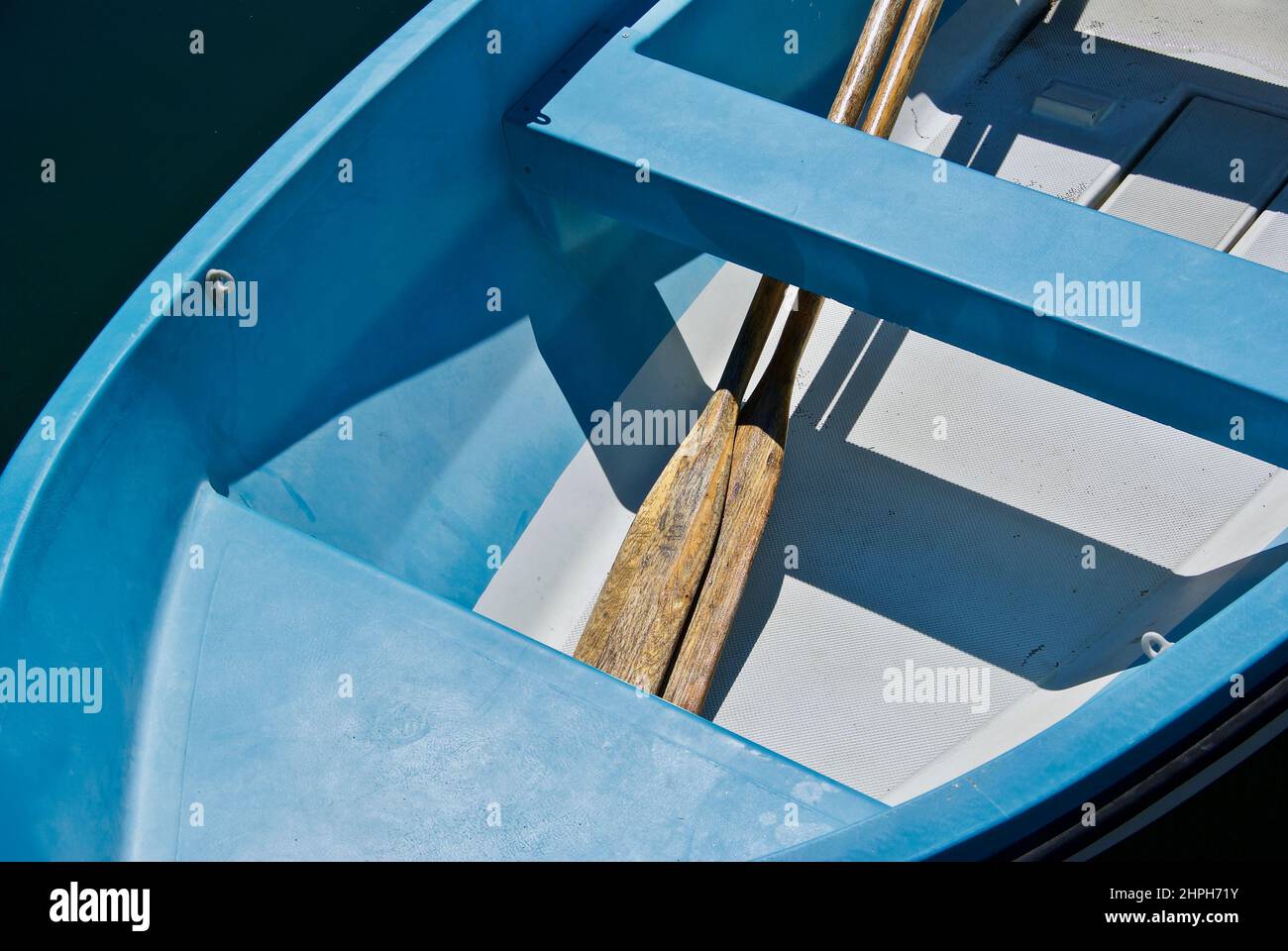 Blue rowing boat with shadow image and two oars laying under seat board. Stock Photo