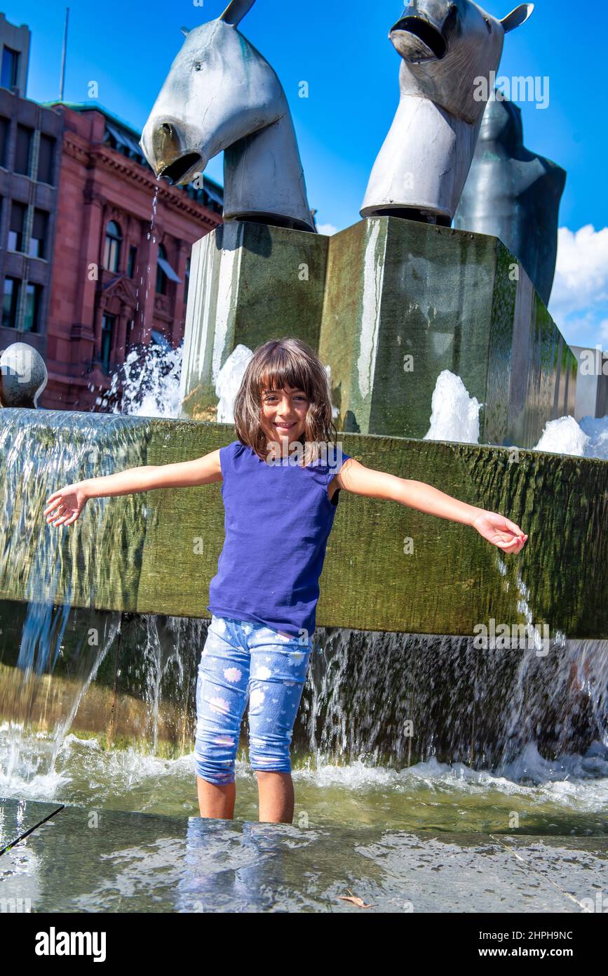 Young girl refreshing in a city fountain protecting from summer heat Stock Photo