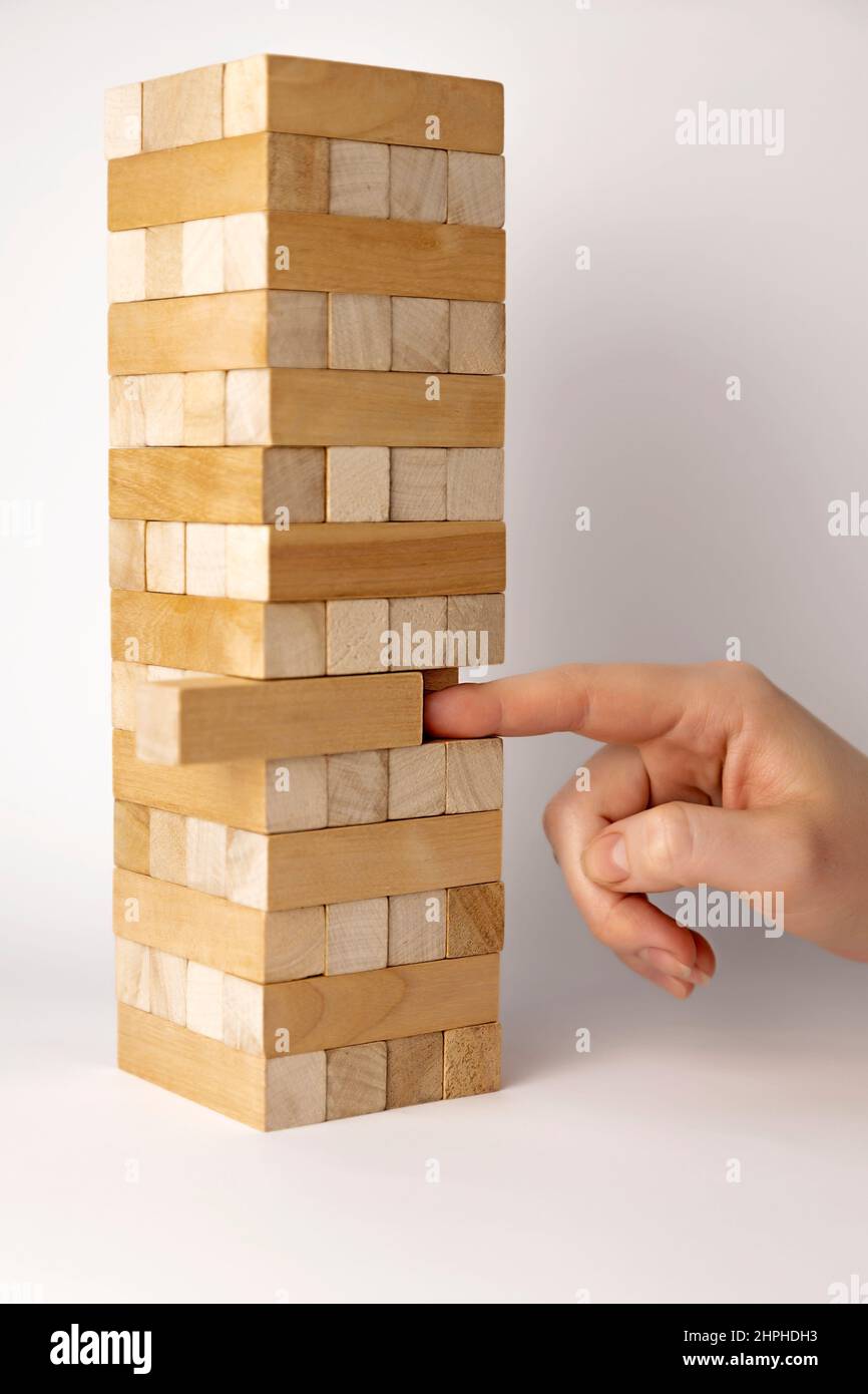 Tower of wooden beams. Finger pushing a wooden beam. Development concept. Jenga board game at home. Stock Photo