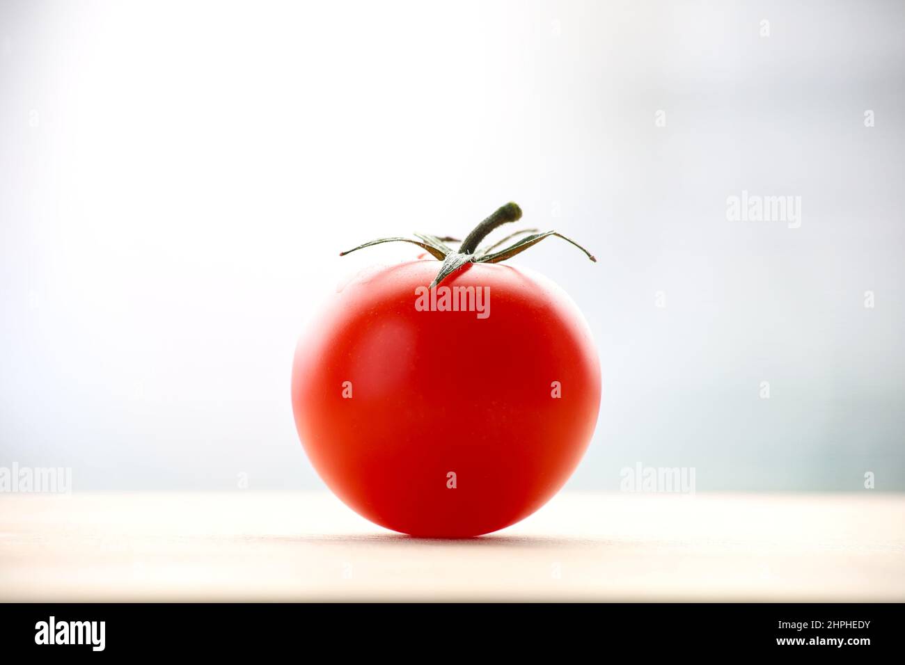 Fresh ripened red tomato on cutting board. Side view with bright bullred background. Stock Photo