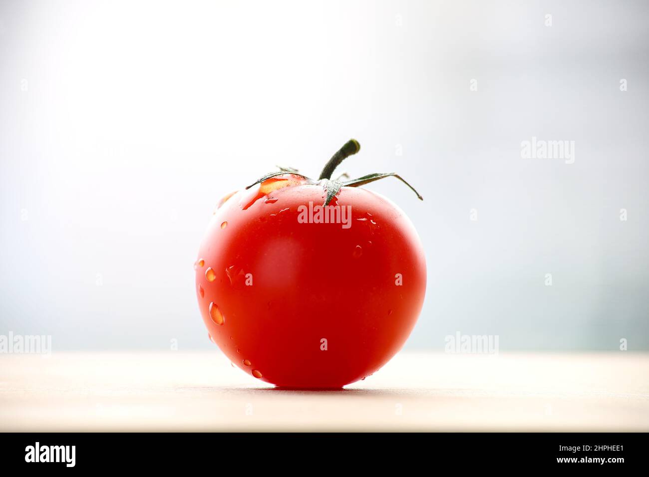 Fresh ripened red tomato on cutting board. Side view with bright bullred background. Stock Photo