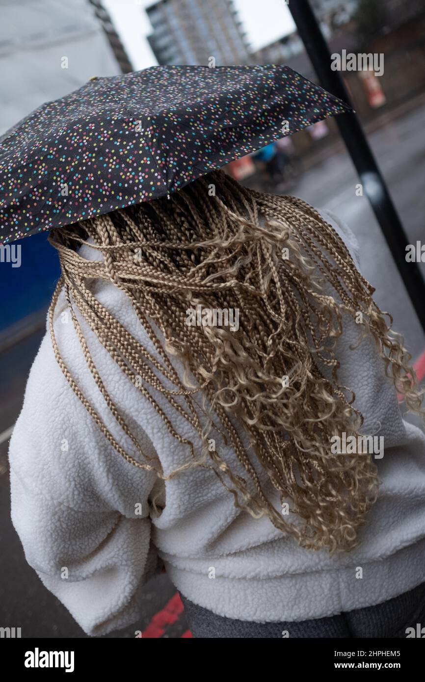 Woman with beautiful hair waits patiently under an umbrella to cross the road road in London Stock Photo