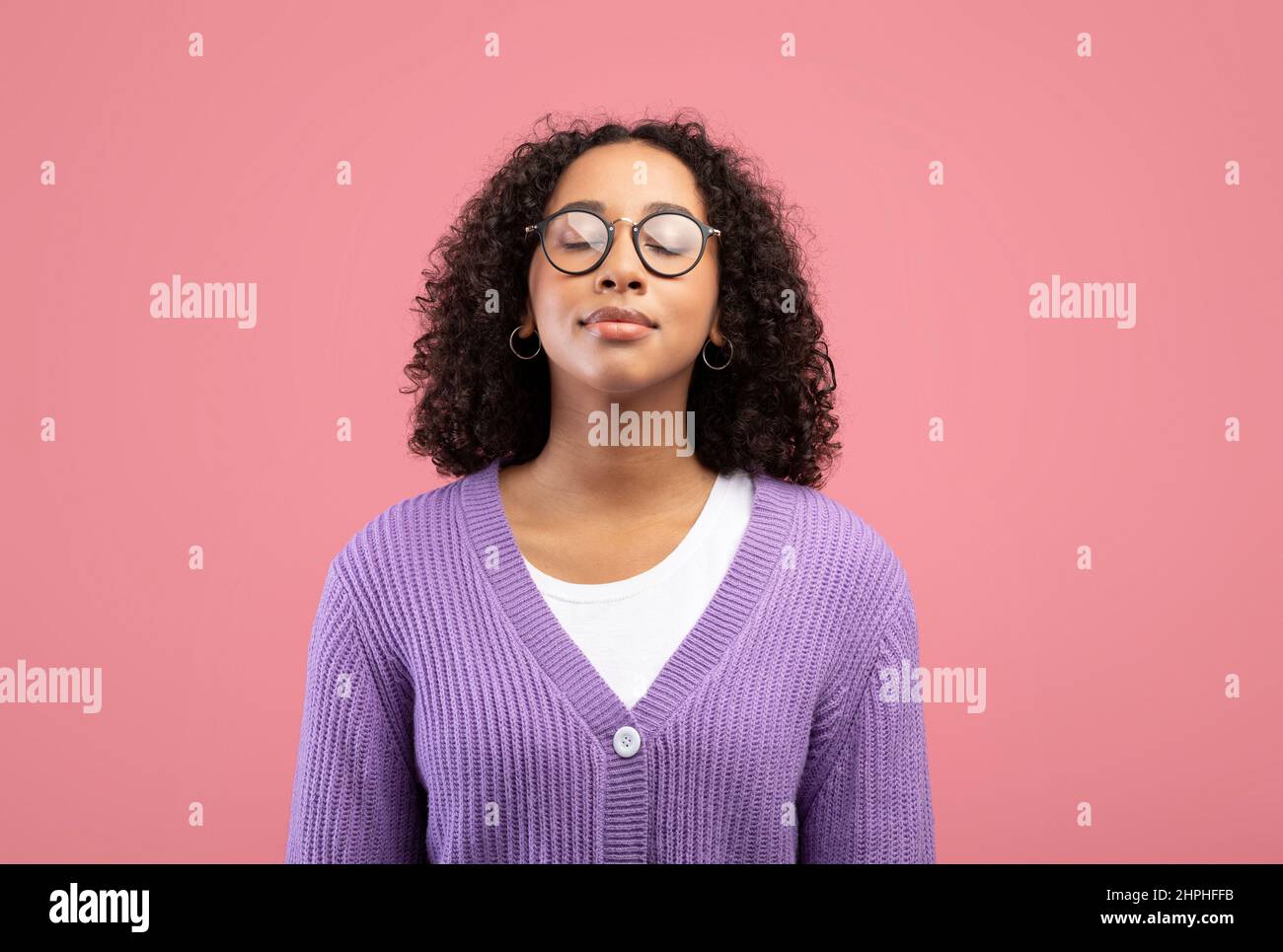 Calm young black woman in glasses closing her eyes, breathing freely on pink studio background Stock Photo