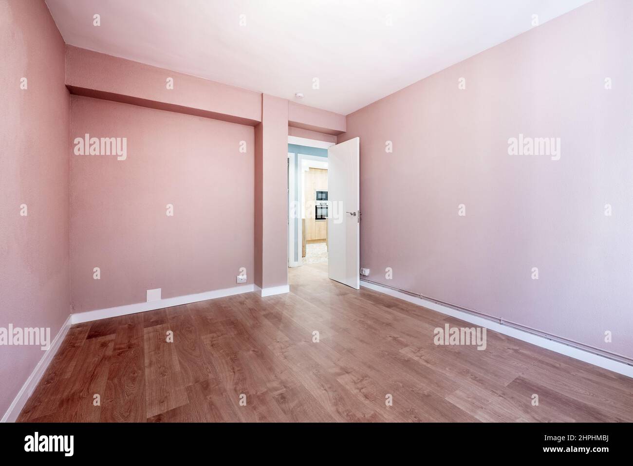 Empty room painted with pastel pink paint, wooden floor, white wood carpentry and white wooden door Stock Photo