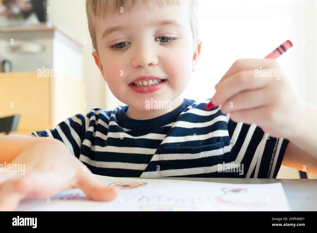 Preschool Age Boy Holds Red Crayon in Hand While Drawing Stock Photo
