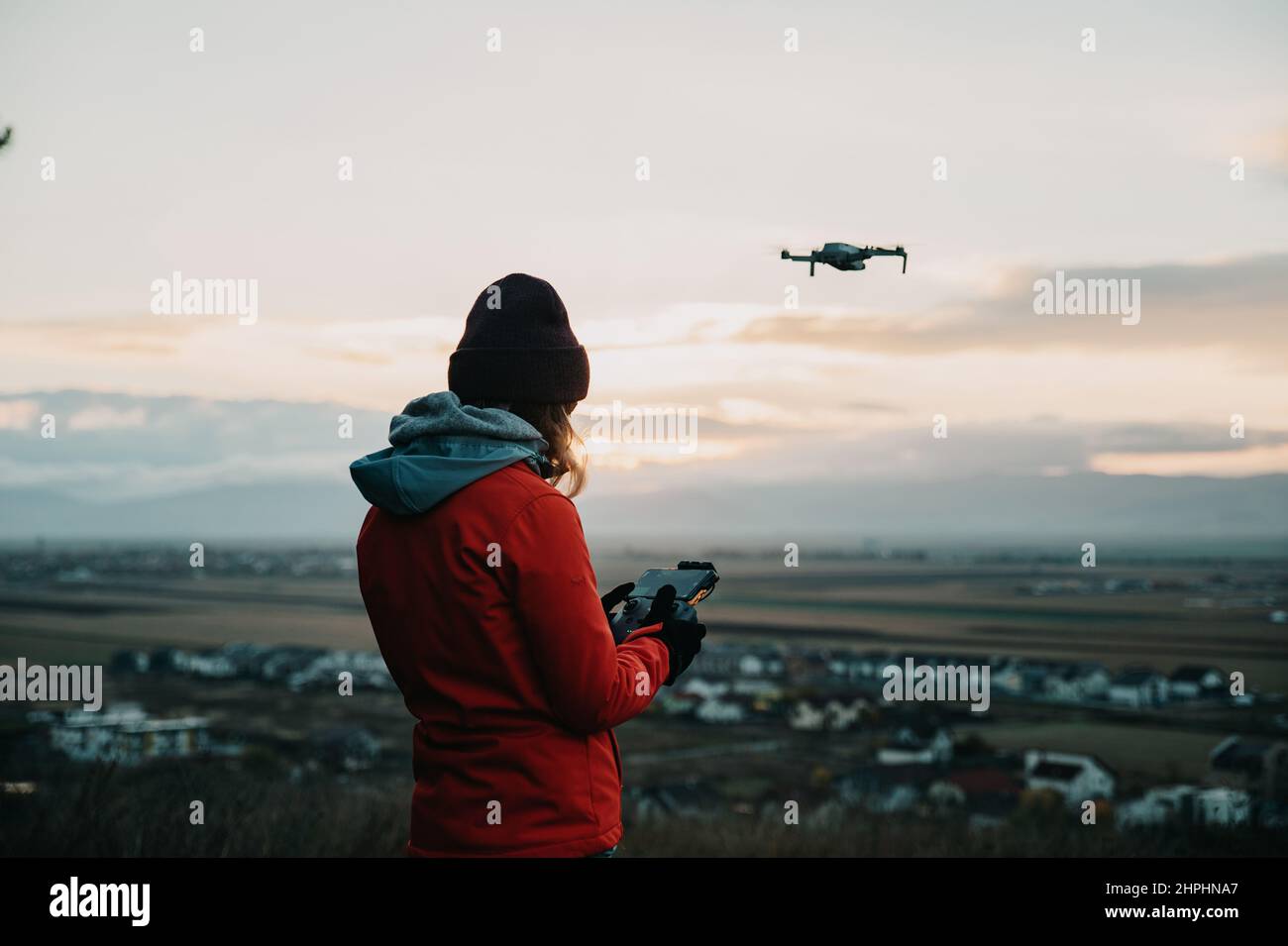 Female pilot using remote controller to fly the drone at sunset Stock Photo
