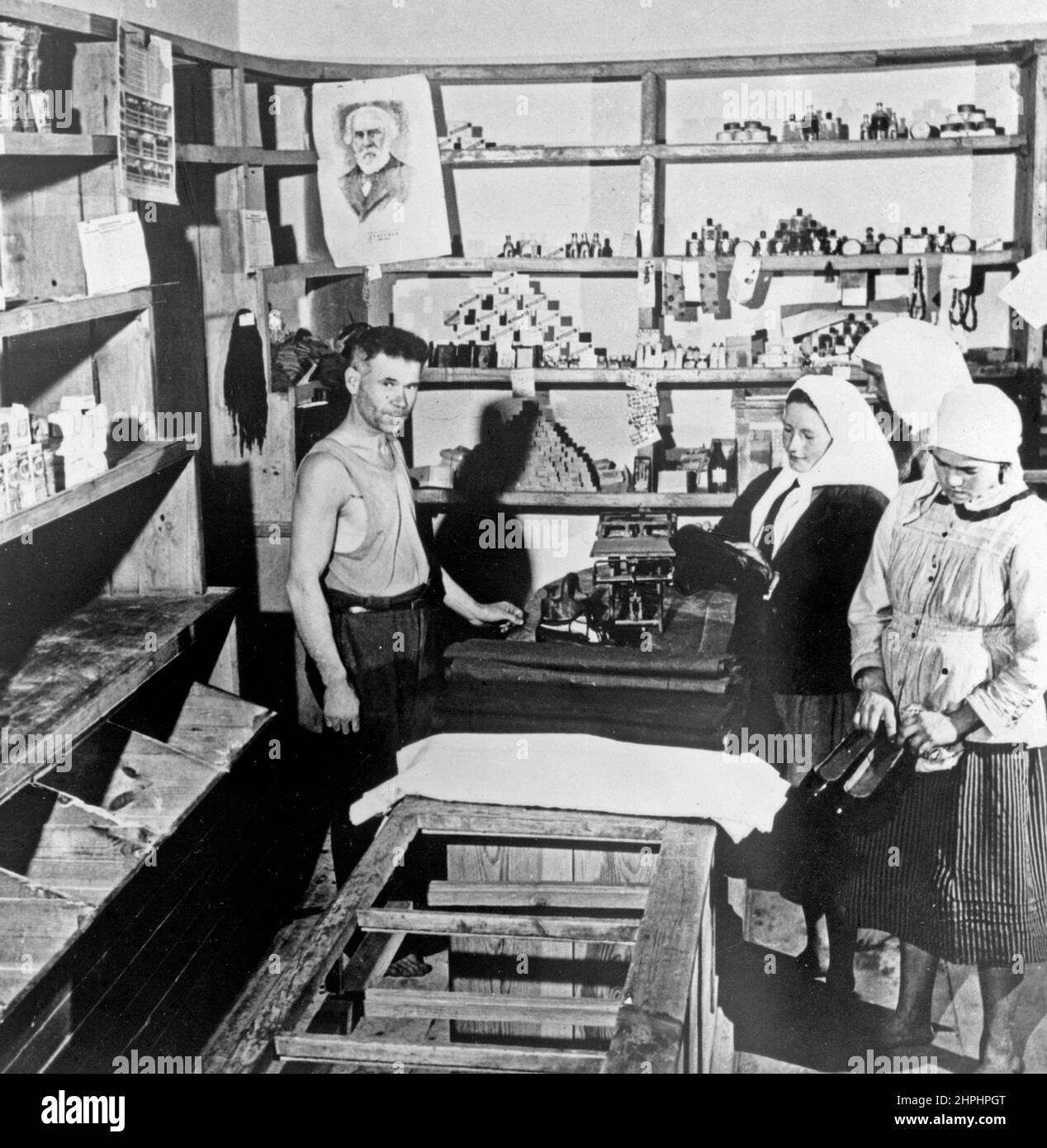 Original caption: Shoes are scarce in workers paradise. Soviet farm women in the Ukraine look at a consignment of over-shoes just received at the village store. Such shipments are scarce and are eagerly awaited. Notice the empty bins and shelves in the foreground. ca.  1951 Stock Photo