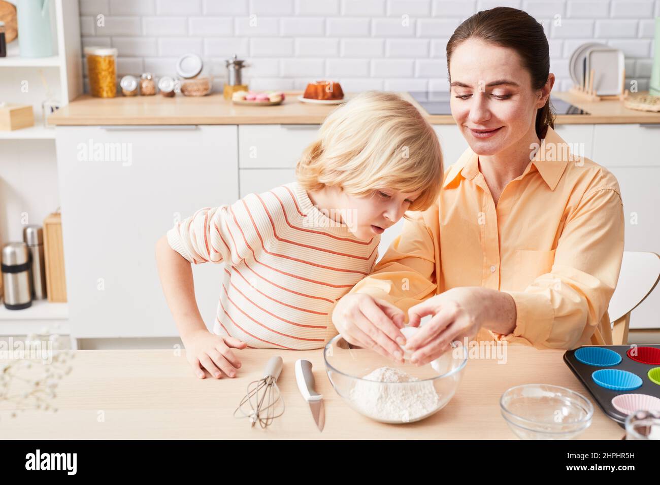 Adorable little boy and his mom in white aprons cooking together in the  kitchen Stock Photo