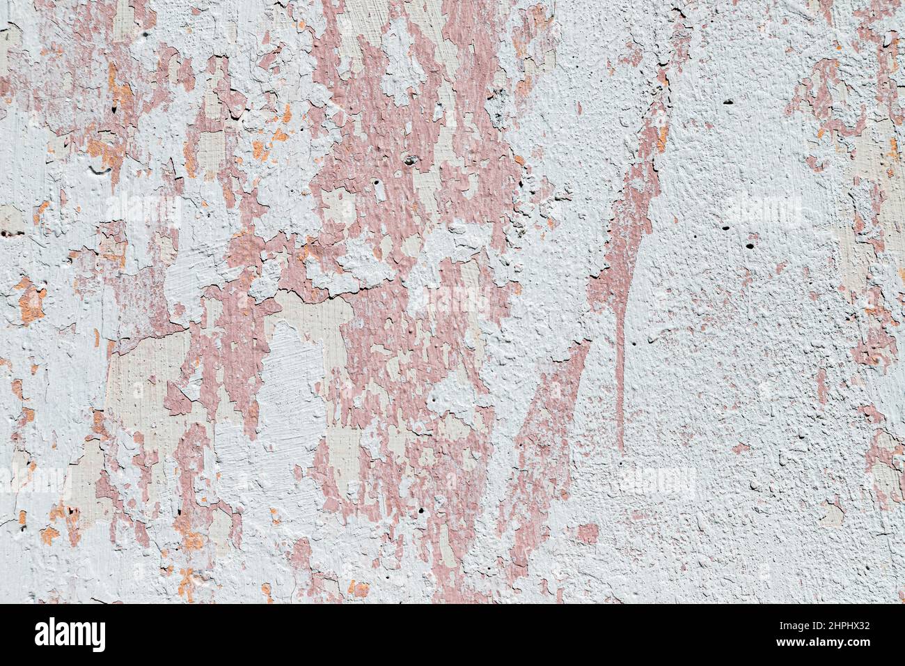 An old concrete wall with peeling paint. Old, dirty, pink-and-white wall, textured background to overlay the design. Stock Photo