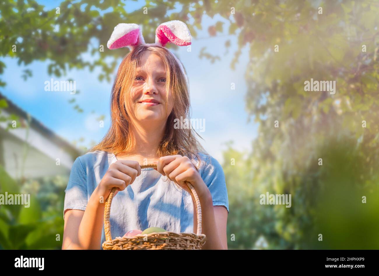 Portrait of a teenage girl in bunny ears with an Easter basket with eggs in the backyard Stock Photo