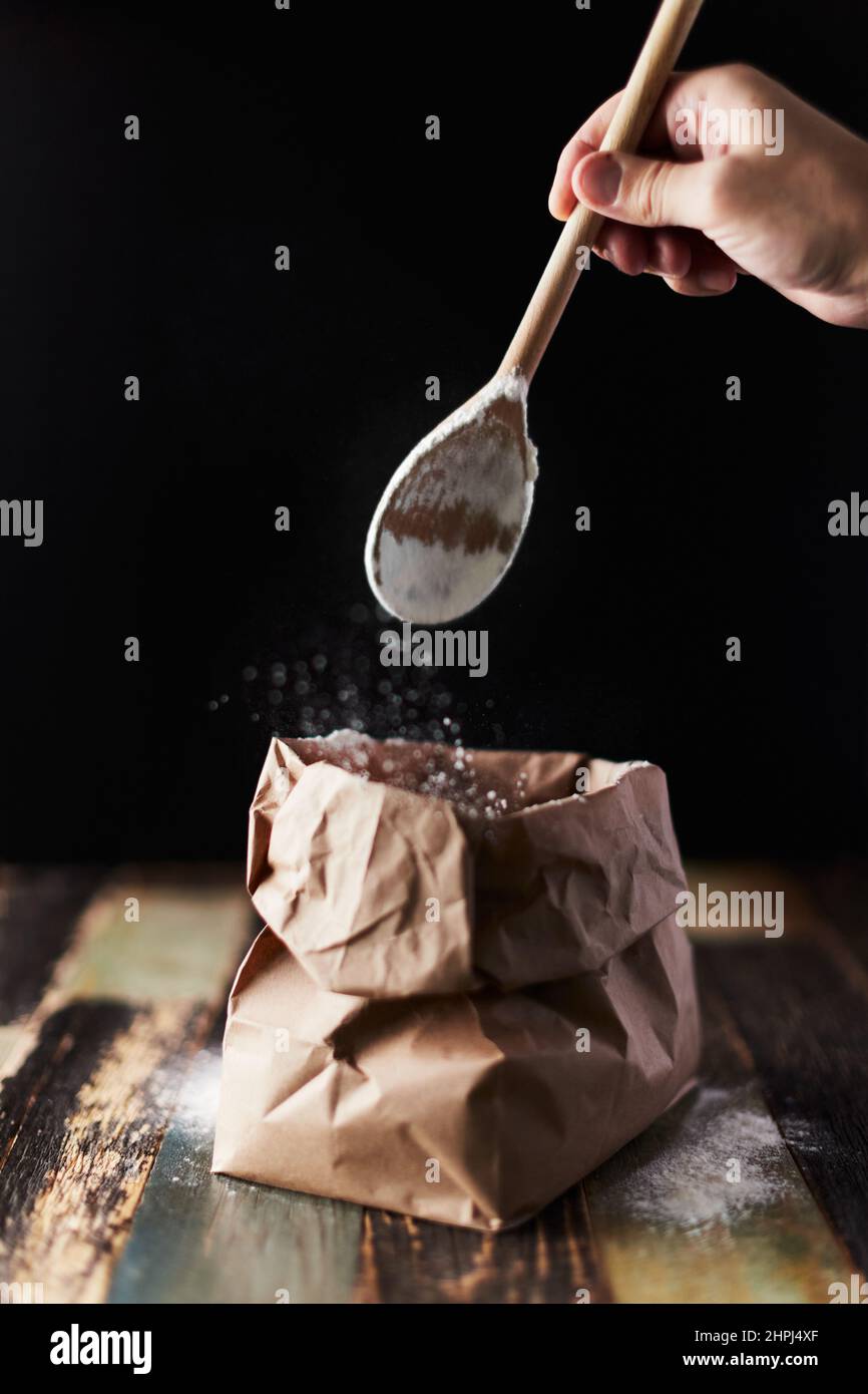 Wheat flour in a craft package. Freeze movement, spoon dark background, sprinkle flour. Front view. Stock Photo