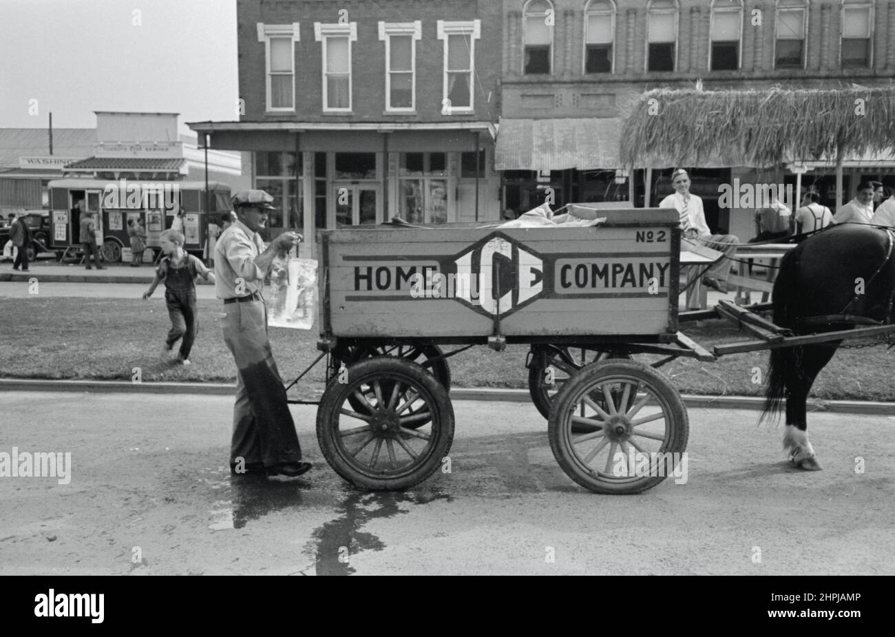 Russell Lee - Delivering ice to National Rice Festival, Crowley Louisiana, Shows iceman holding block of ice in tongs behind horse drawn ice wagon. Stock Photo