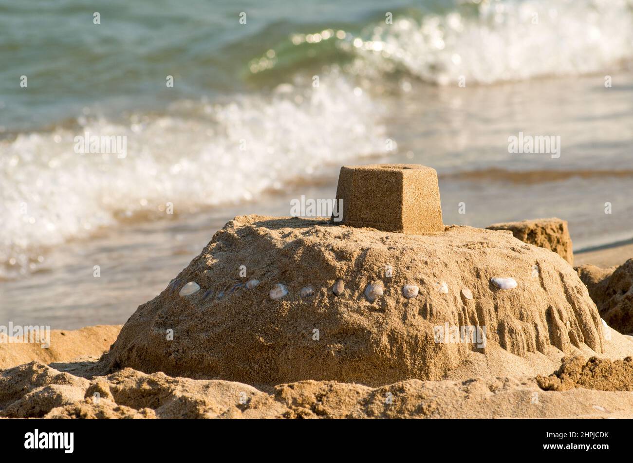 Sand castle on the seashore and a soft blue sea wave.  Sunny blue sea , sand castle on the beach. Ocean water , blurred background. Stock Photo
