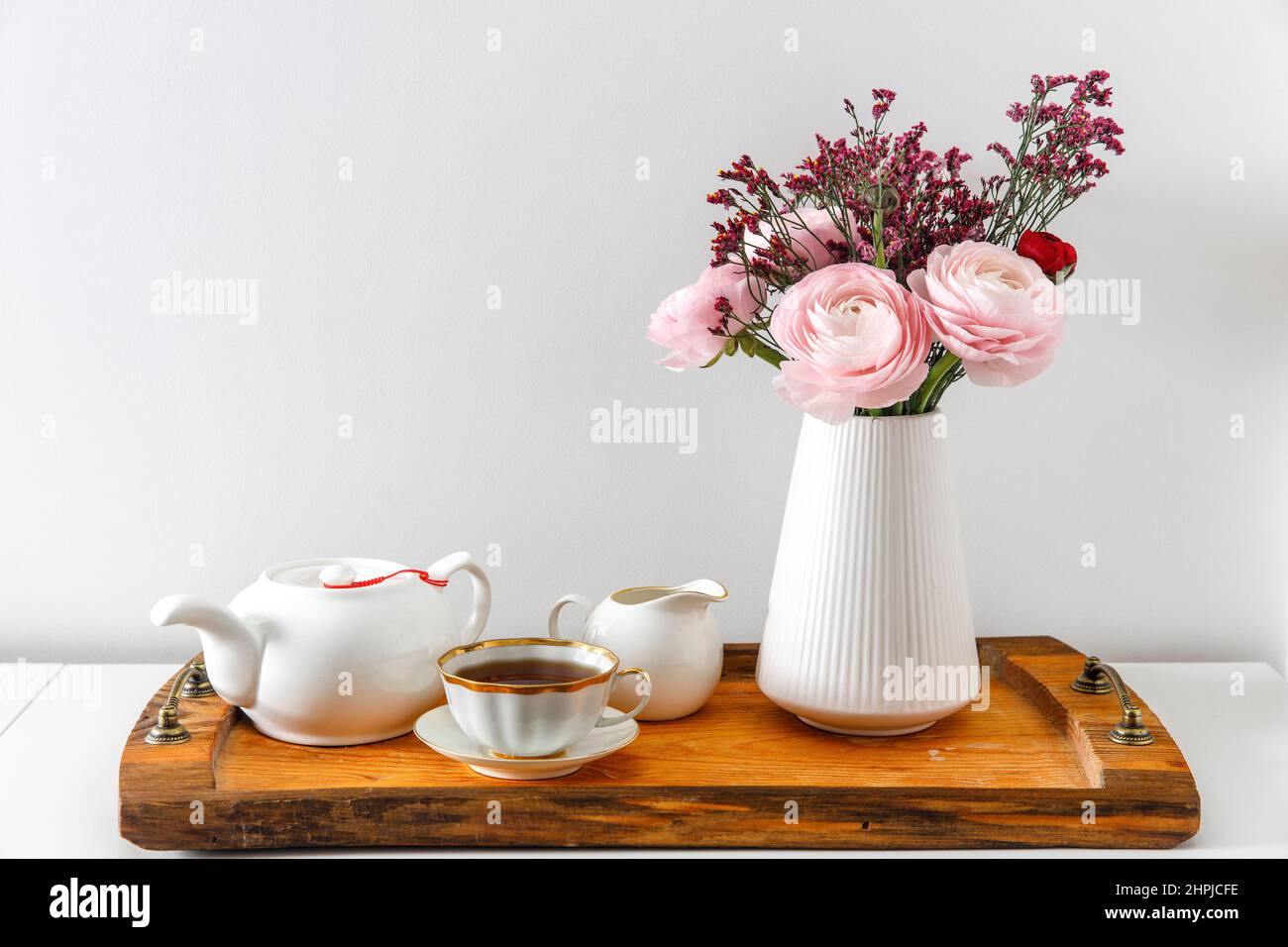 Persian pink buttercup with the wooden brown tray on a white table. Time to drink tea. Ceramic teapot and two porcelain cups. Copy space Stock Photo