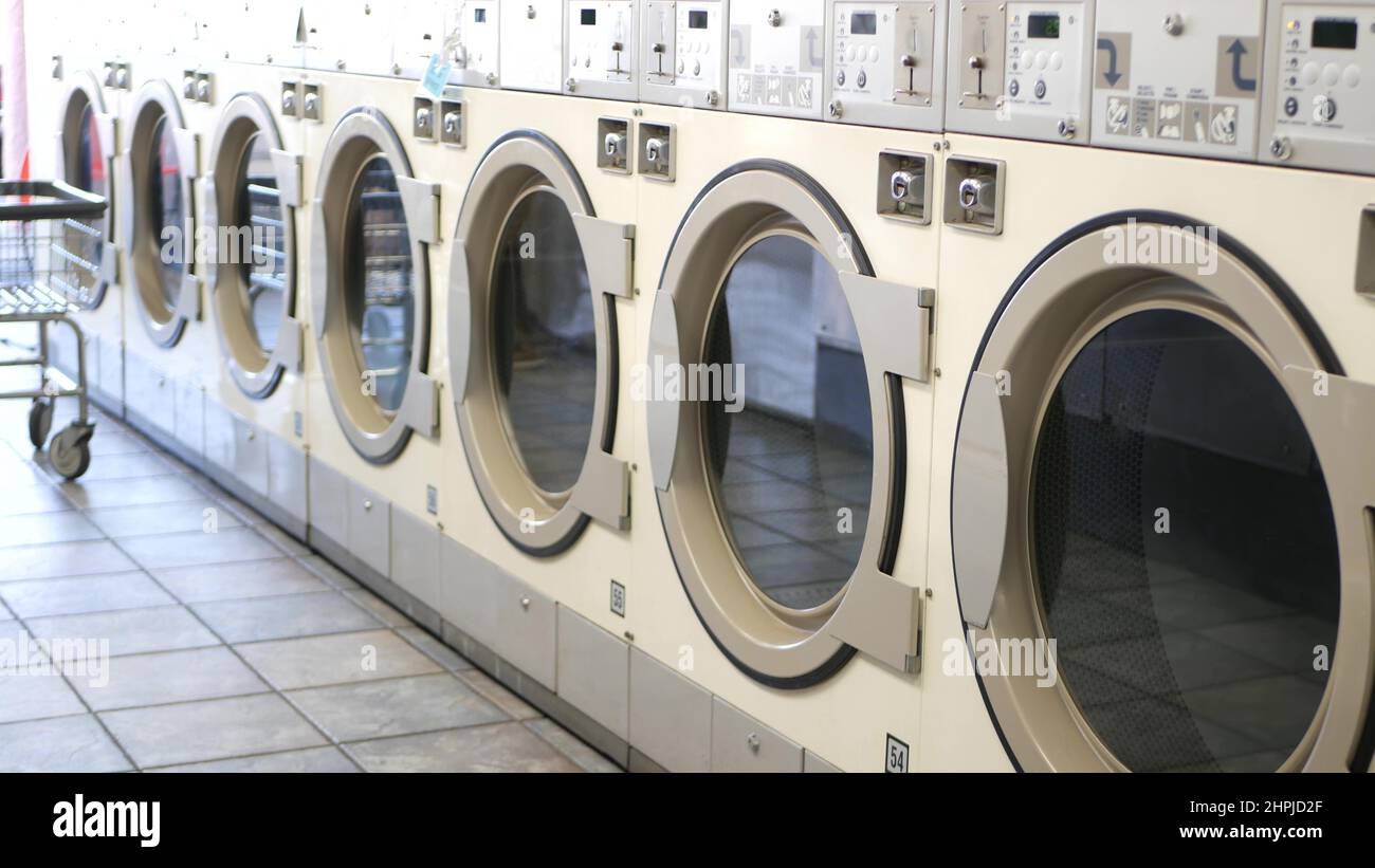 Row of washing and drying machines, public coin laundry in California, USA. Drums of washers and dryers in self-service laundromat or commercial laundrette. Automatic launderette in United States. Stock Photo