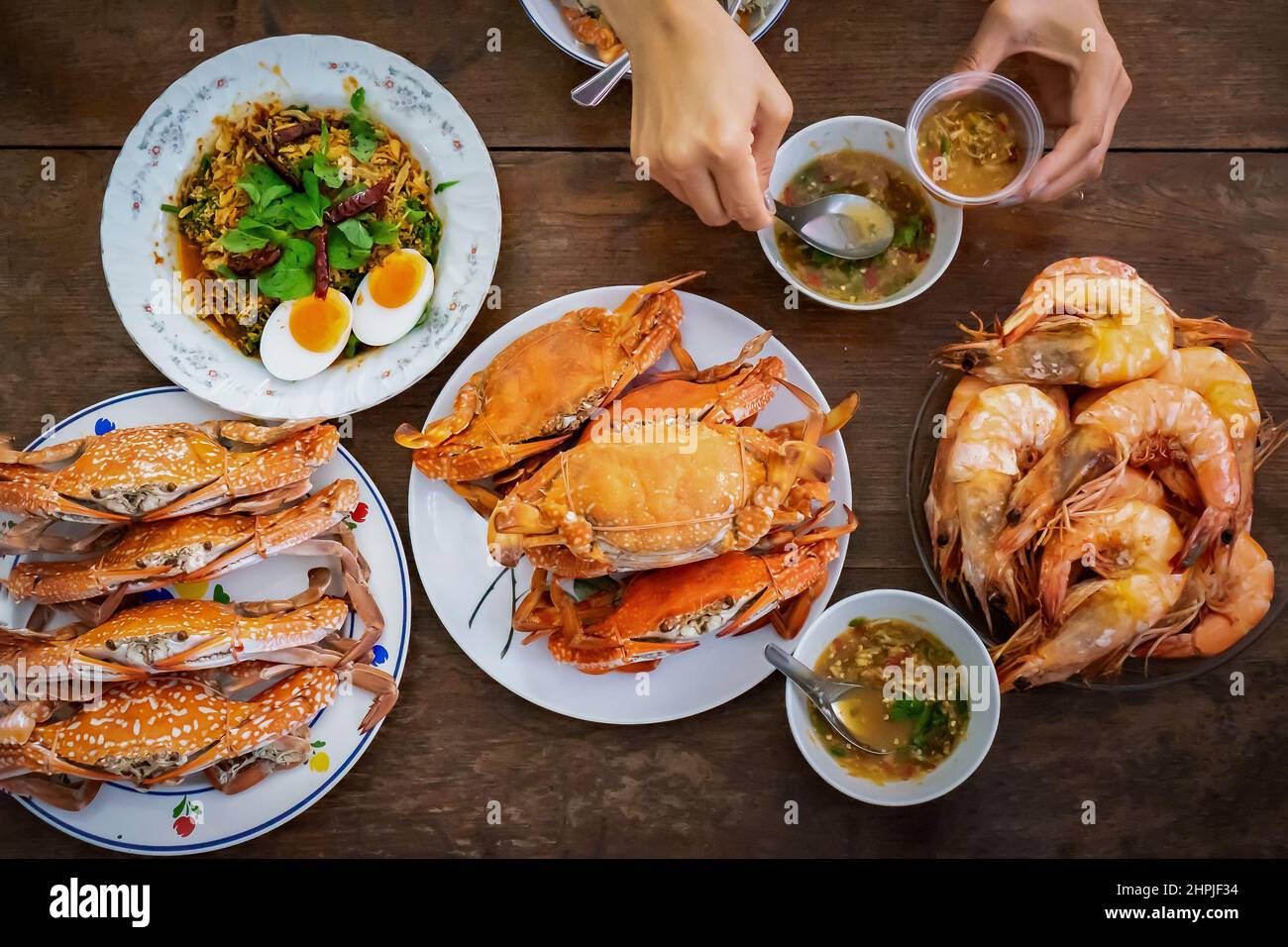 Top view Steamed Crabs and Shrimps set on the vintage wooden table with the the Asian hand picks up seafood sauce above of it before they eat. Stock Photo