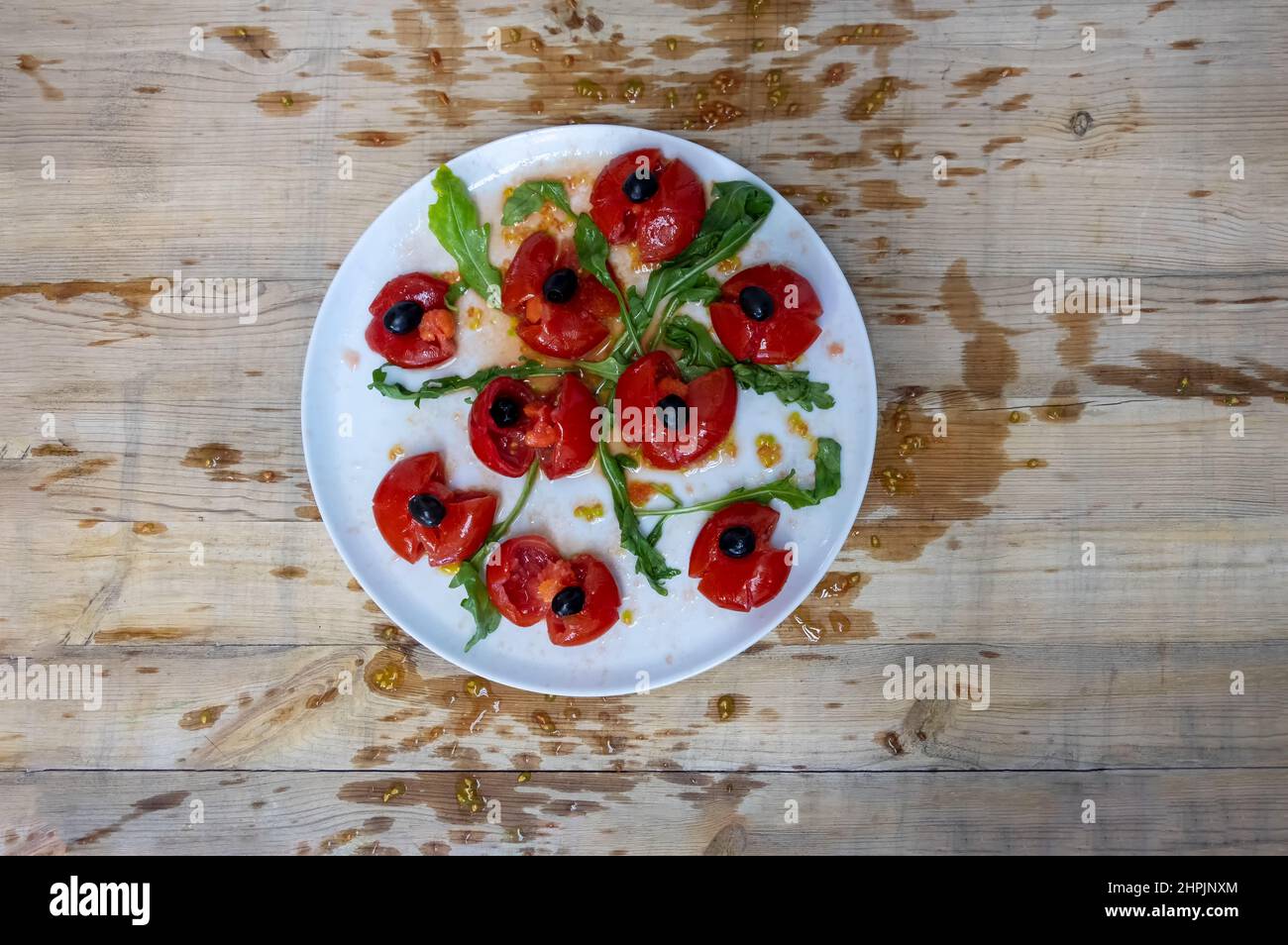 Tomatoes smashed with a fist, decorated with black olives and arugula arranged on a wooden table, the pulp splattered wildly, are supposed to represen Stock Photo