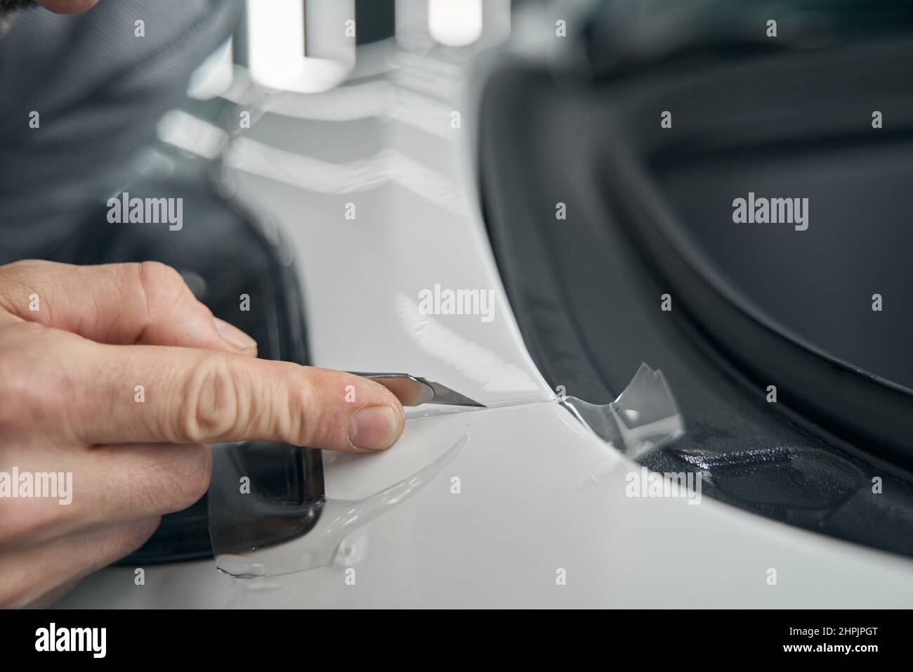 Skilled worker removing excess PPF on auto body panel Stock Photo