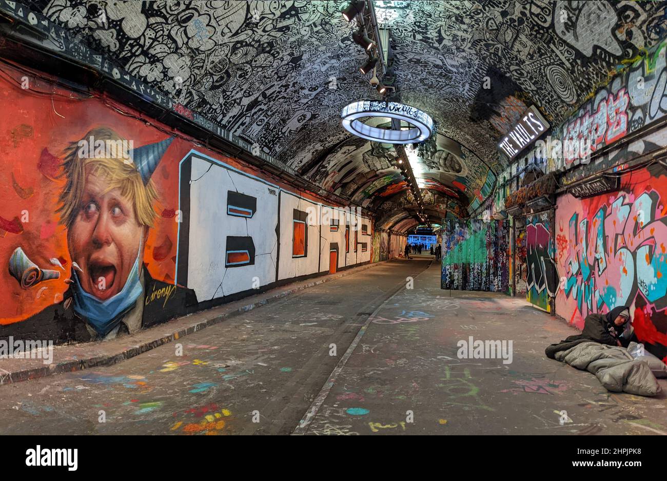 Graffiti depicting the UK Prime Minister Boris Johnson having a party contrasts with a homeless person sleeping rough on the pavement opposite Stock Photo
