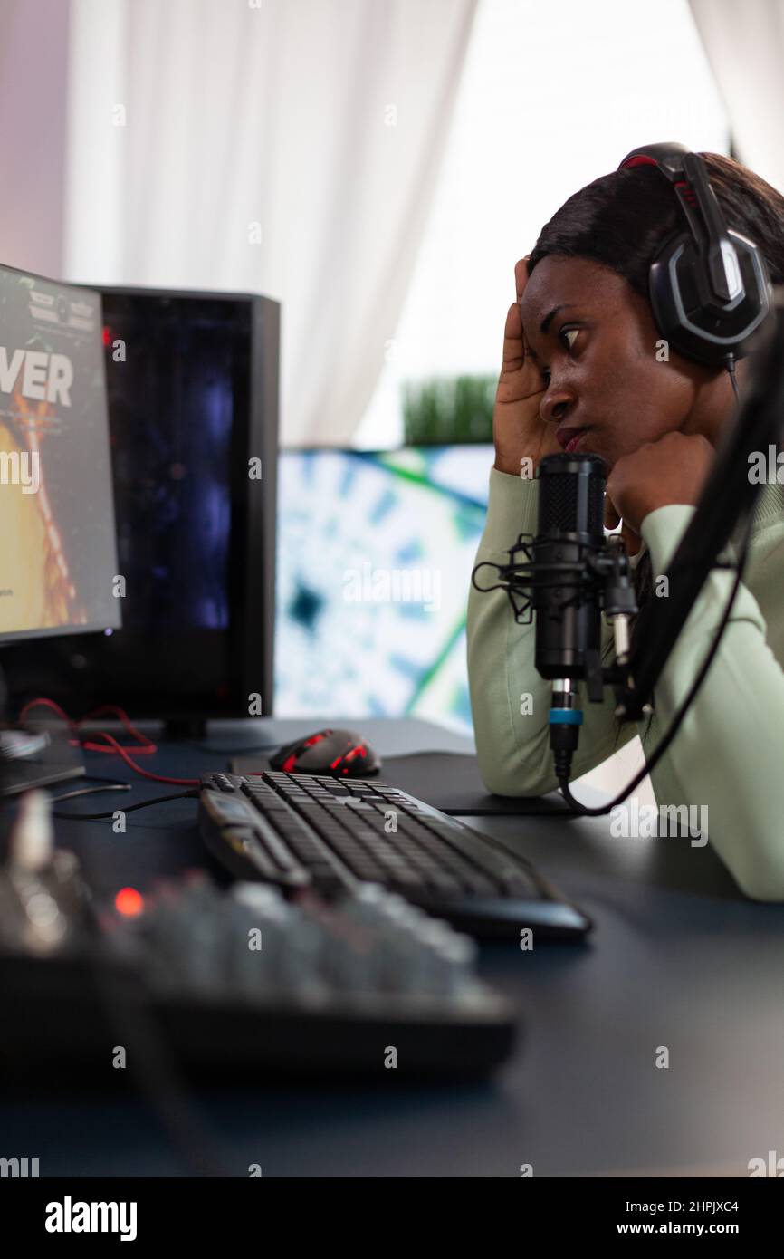 Upset sad esport gamer losing space shooter videogames using RGB computer, gaming for online championship. Nervous woman player with headphones talking with remote player using live streaming Stock Photo